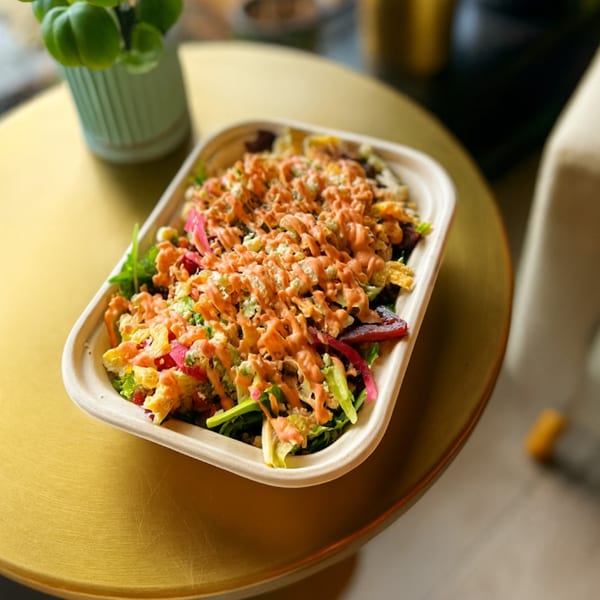 A colorful salad with orange dressing in a rectangular container on a gold table.