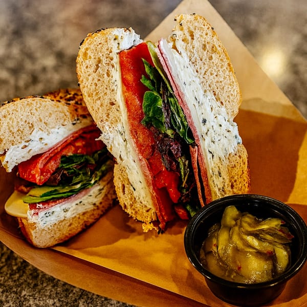 Two halves of a deli sandwich with meat, cheese, lettuce, and tomato, with a side of pickles.