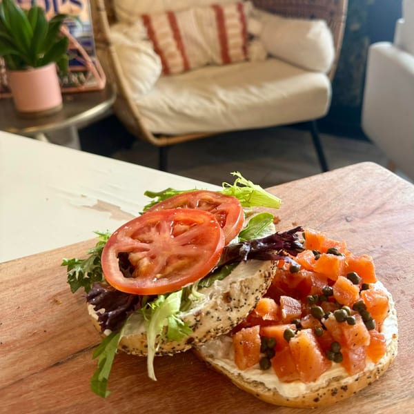 Two everything bagels with cream cheese, one with lox and capers, the other with lettuce and tomato.